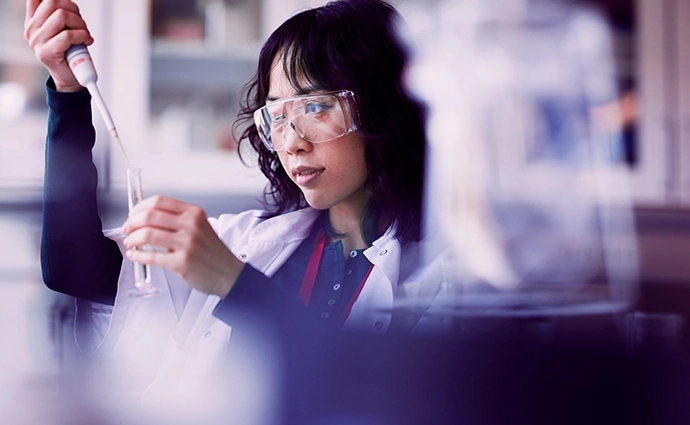 A woman working in a lab, collecting a sample in a glass tube for analyzing.