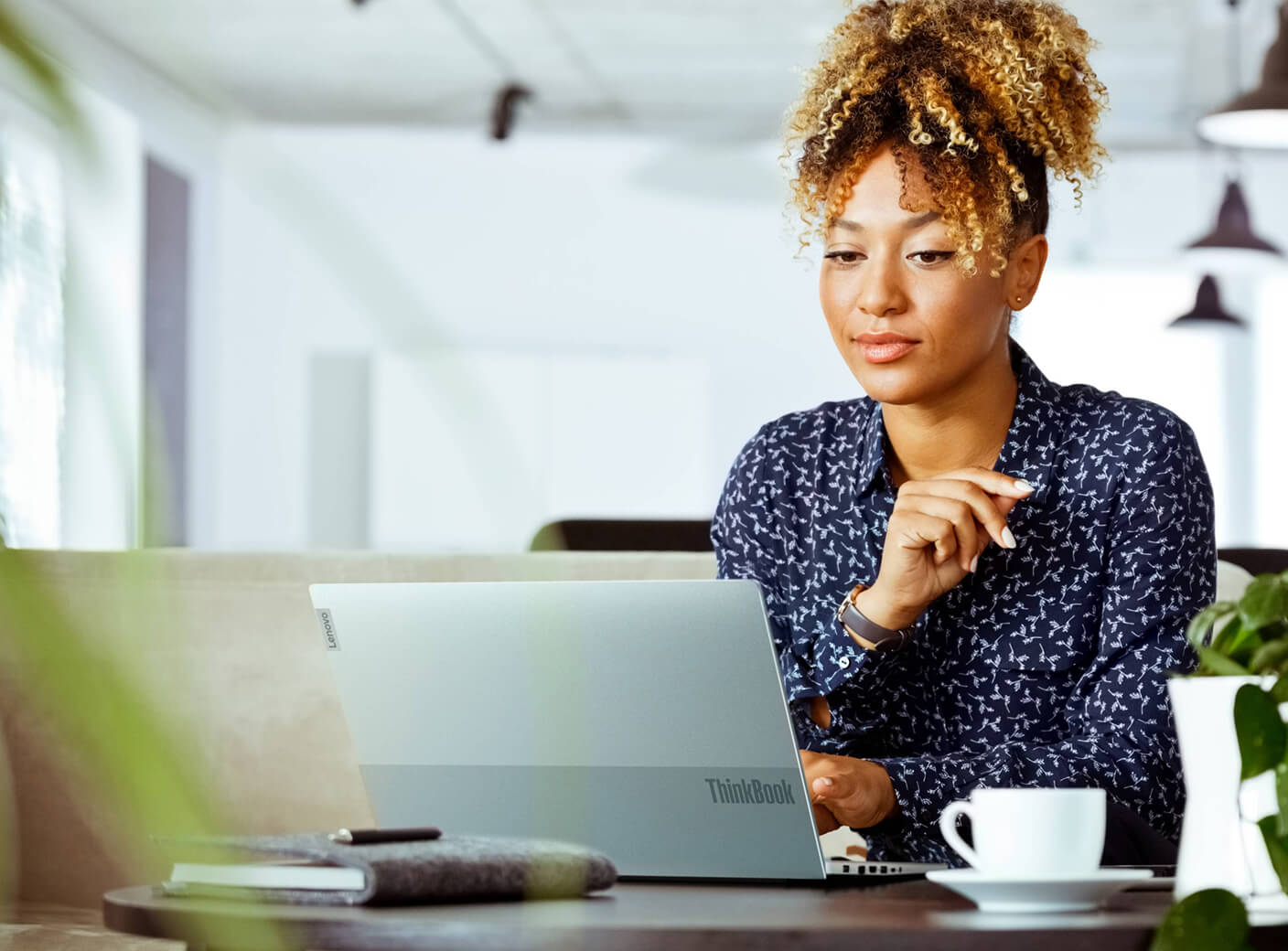 A woman working on her laptop in the office with a cup of coffee.
