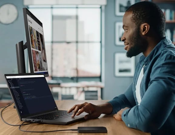 Person sitting at desk in home studio, facing ThinkPad E14 Gen 5 (14, intel) laptop and using trackpad to navigate files