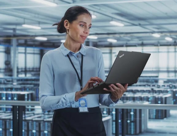 Person standing in data center, holding ThinkPad E14 Gen 5 (14, intel) laptop in one hand and looking at the display