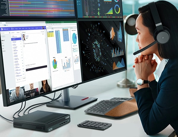 Someone looking at financial charts on a bank of monitors alongside a Lenovo ThinkCentre M90q Gen 4 Tiny Intel PC while on a video conference call