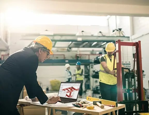 Person wearing a hardhat and standing at a makeshift desk inside a partially constructed building, looking at building plans on a ThinkPad P14s Gen 4 (14