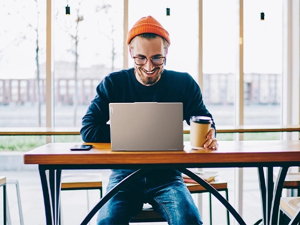 Front view of a person sitting in a café and working the Lenovo IdeaPad 5 2-in-1 Gen 9 (14 inch AMD) laptop in Luna Grey placed on the desk.