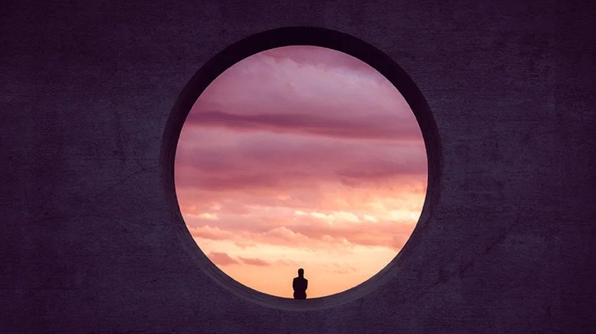Une grande fenêtre ronde avec un beau coucher de soleil et une personne silhouettené à l’extérieur