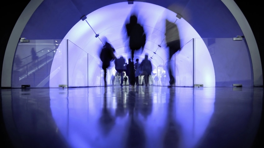 Blurs of people walking through a tunnel filled with blue light 