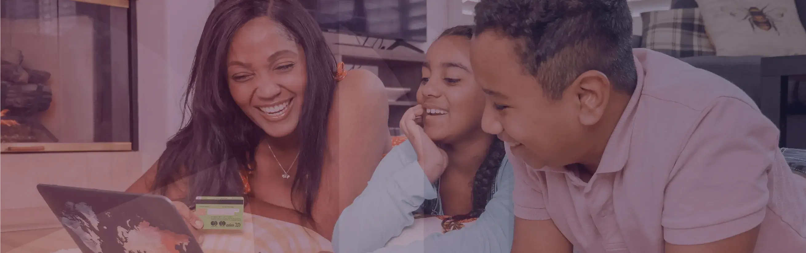 An adult holding a credit card and two children smile and laugh while looking at a laptop display.