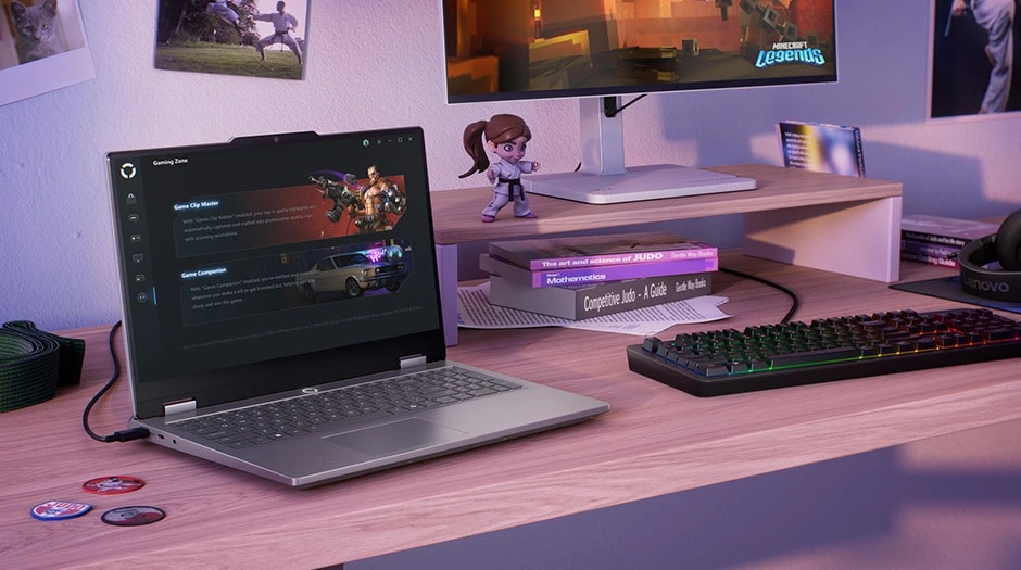 Lenovo LOQ Essential 15IRX11 gaming laptop on a desk with mouse, keyboard, mousepad, and monitor – left-front view, lid open, with Legion Space “Gaming Zone” screen on the display.