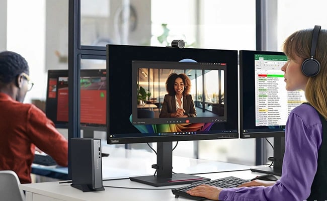 A woman in a call center types on a keyboard in front of a dual-monitor Lenovo ThinkStation setup.