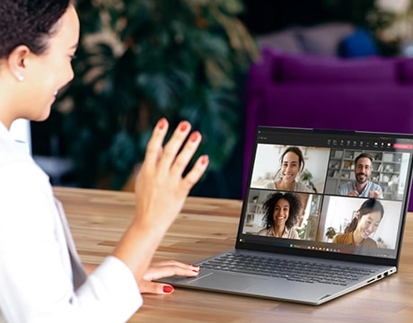 Über-der-Schulter-Ansicht einer Frau, die bei einem Videoanruf sitzt und winkt, mit dem Lenovo ThinkBook 16 Gen 9 Notebook.