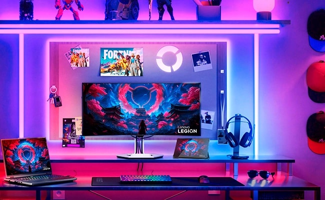 A glass desk with elements of the Legion ecosystem, including a laptop, monitor, tablet, headphones, and a wireless keyboard and mouse.