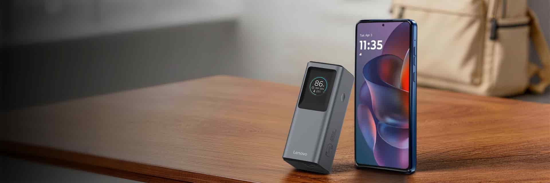 A small Lenovo device beside a smartphone on a wooden surface.