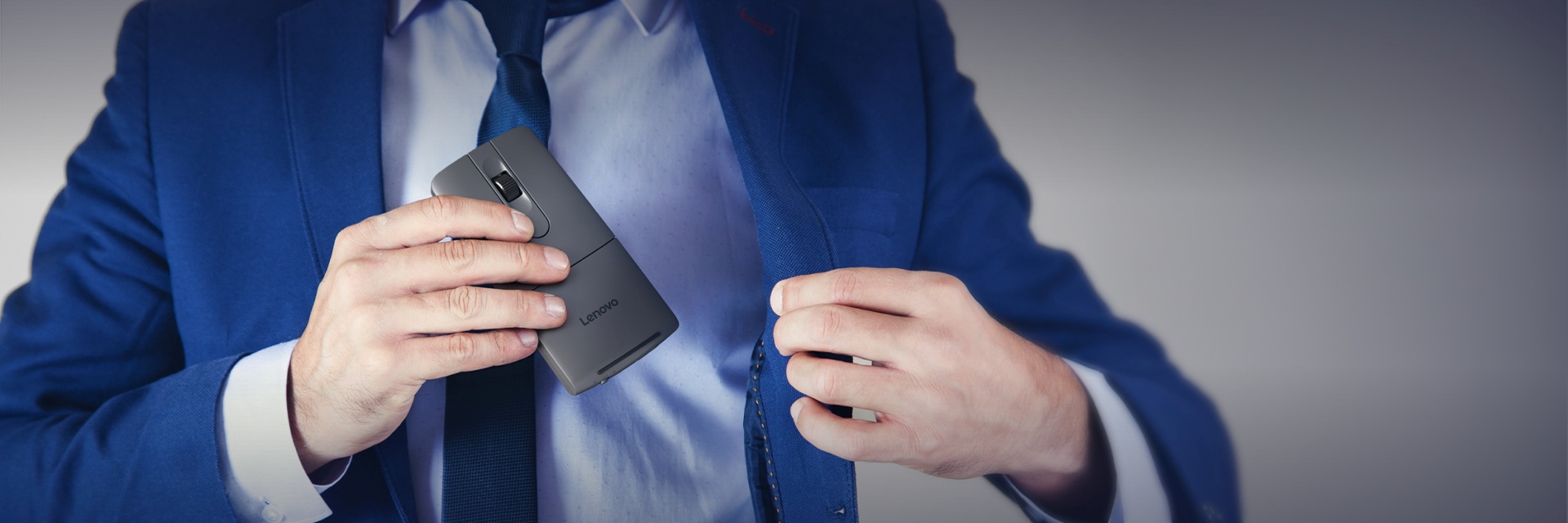 A person in a blue suit sliding a slim, foldable Lenovo device into a suit pocket.