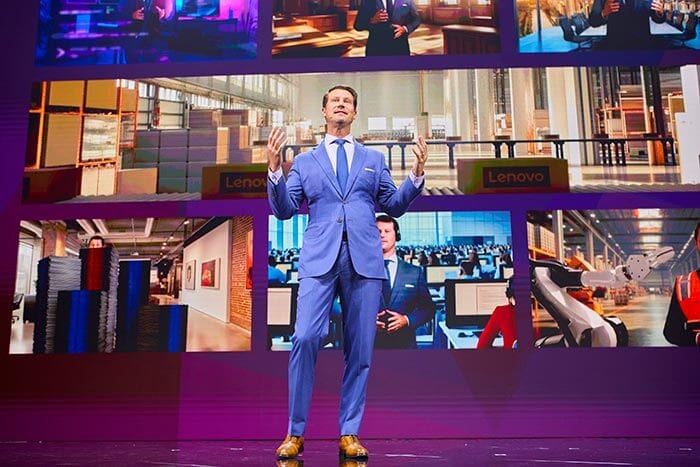 Matt Zielinski in a blue suit stands in front of a screen displaying multiple business and tech scenes.