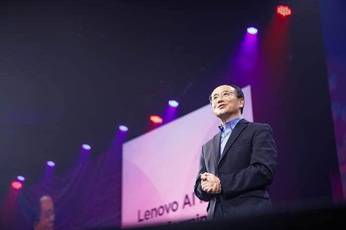 Dr. Yong Rui in a suit speaks on stage at a Lenovo AI-related event, with focused lighting.