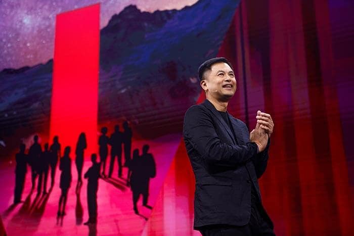 Ken Wong no palco com uma silhueta de pessoas contra um fundo vermelho e escuro impressionante.