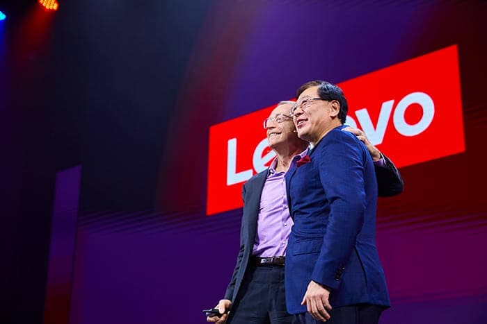 O CEO da Lenovo, Yuanqing Yang, e o CEO da Intel, Pat Gelsinger, posando juntos, sorrindo, no palco com um grande logotipo da Lenovo ao fundo.