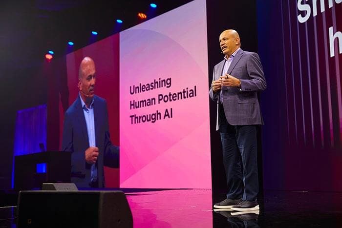 Lenovo CTO, Dr. Tolga Kurtoglu, speaks on stage in front of a screen with text “Unleashing Human Potential Through AI.'