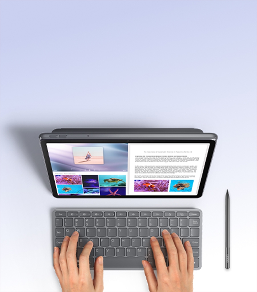 Vista superior de un usuario escribiendo en una tableta Lenovo con el teclado bluetooth y el lápiz digital colocado junto al dispositivo.