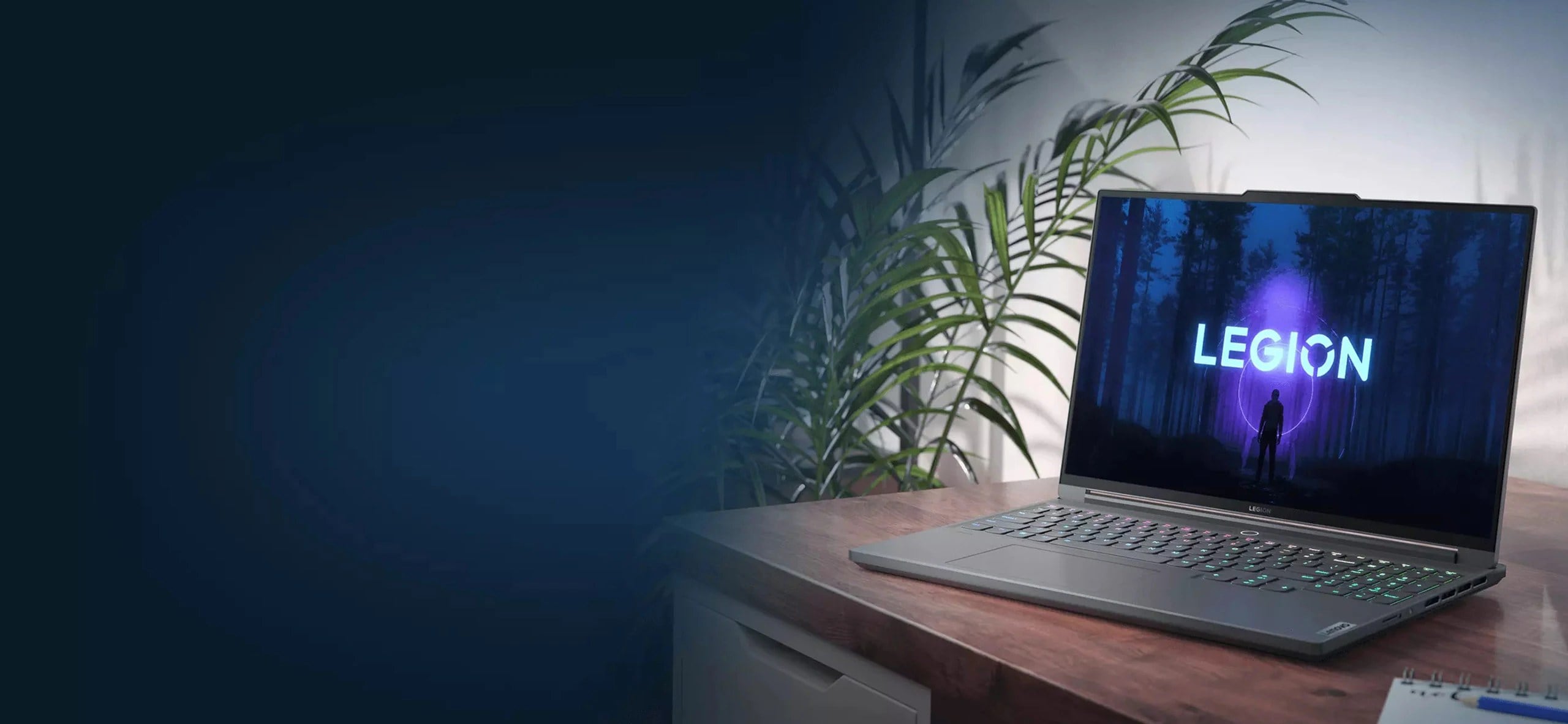 Снимок в три четверти средним планом ноутбука Lenovo Legion Slim 7, установленного на столе и повернутого экраном влево, с видимым на дисплее логотипом Legion и с растениями слева от стола на заднем плане.