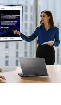 A professional woman presents a slideshow on a ThinkBook laptop to an audience during a meeting.