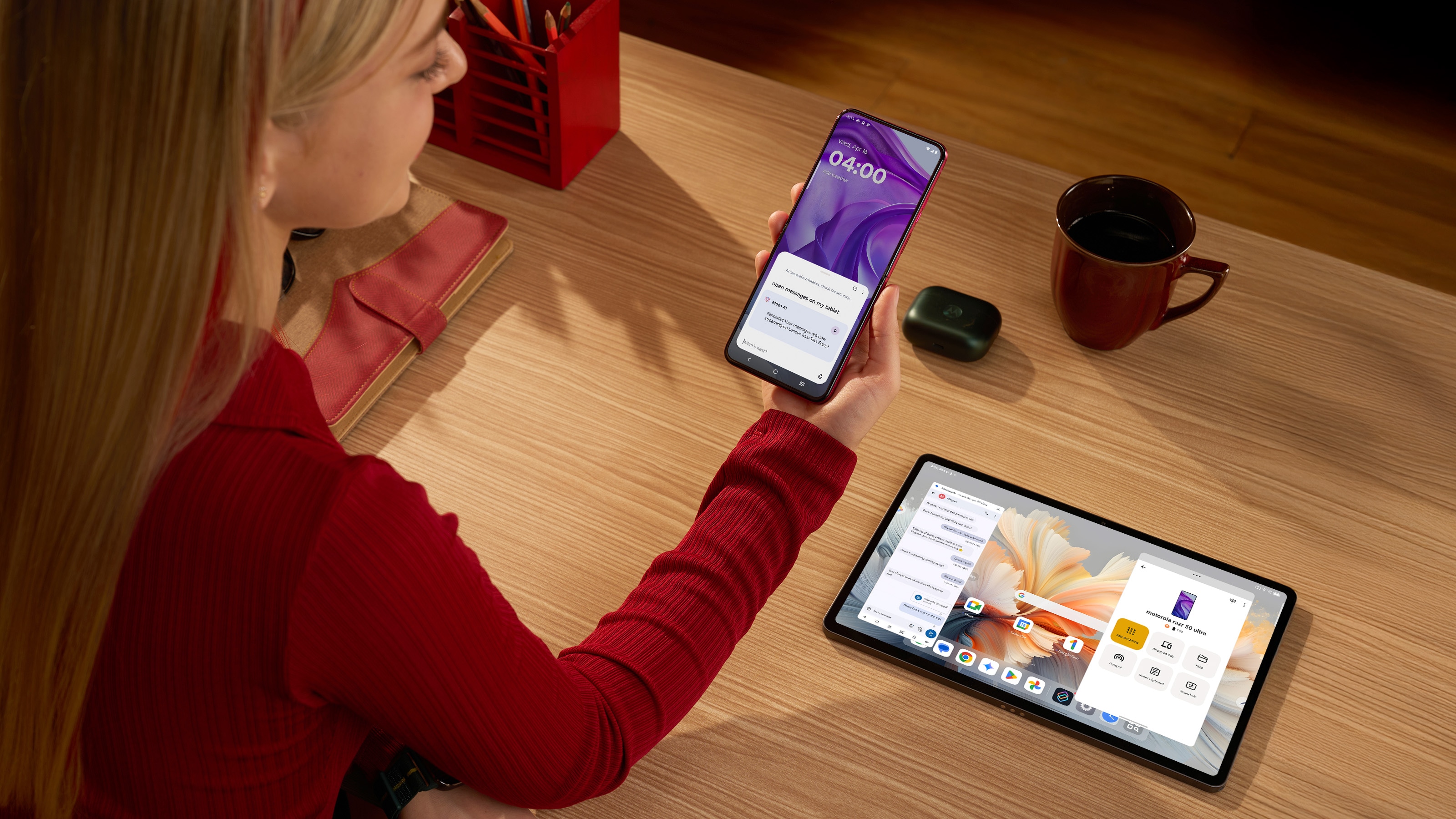 Une personne tient un téléphone Moto affichant l’invite Smart Connect «   ;ouvrir les messages sur ma tablette  ; », tandis qu’une tablette Lenovo sur le bureau affiche l’application de messages et le tableau de bord Smart Connect.