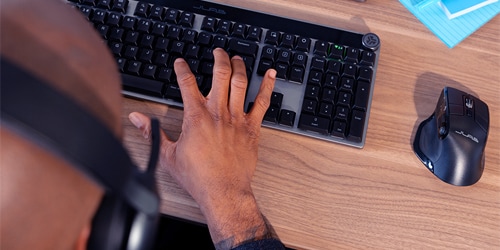 A guy is using a JLab keyboard and mouse at his desk.