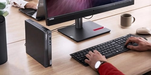 A man working on a desk with a ThinkCentre PC and a Thinkvision monitor