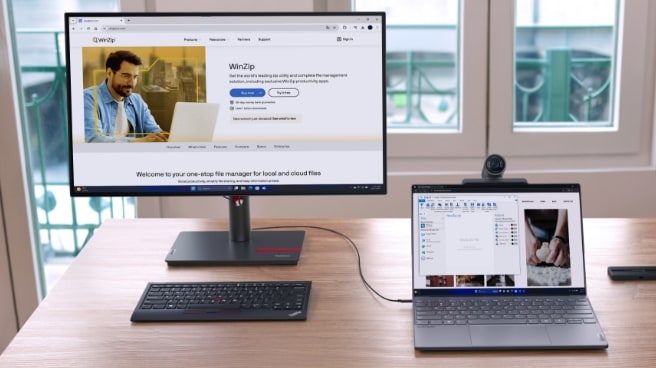a workspace with a Lenovo laptop and an external monitor. The monitor displays the WinZip website, while the laptop screen shows a file manager with various files.