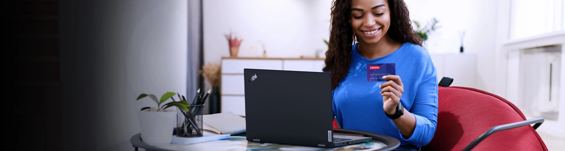 Women sitting in front of a Lenovo ThinkPad laptop and holding a credit card with the Lenovo logo in it