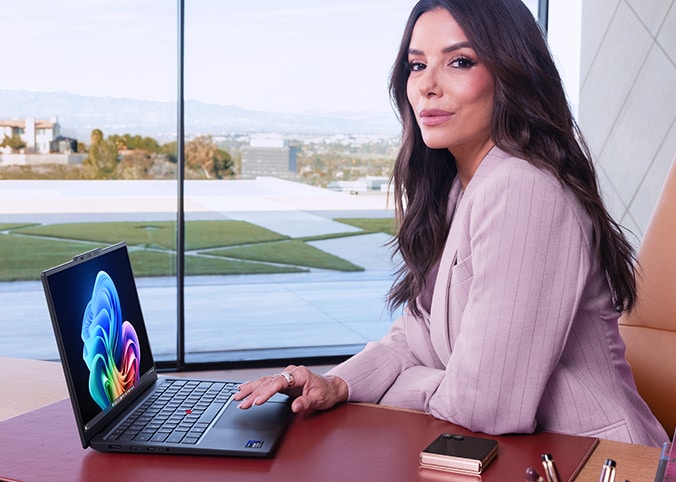 A young woman sitting at a table with a coffee working on her Lenovo laptop. 