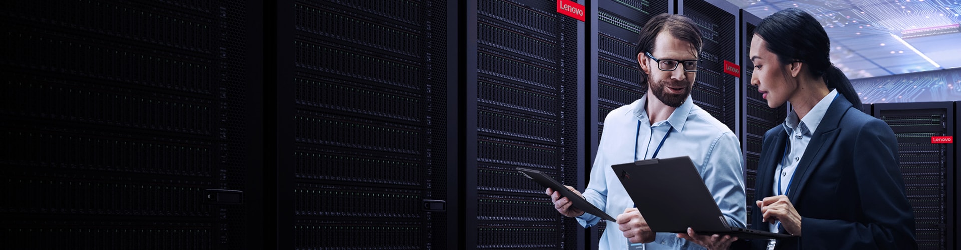 Deux collègues avec des ordinateurs portables et des tablettes traversant une salle de serveurs