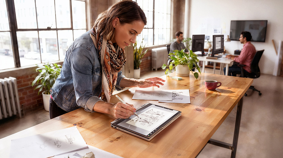 A woman sketches on a display in a collaborative workspace, using the Lenovo ThinkBook 14 2-in-1 Gen 6 laptop in Tablet mode.