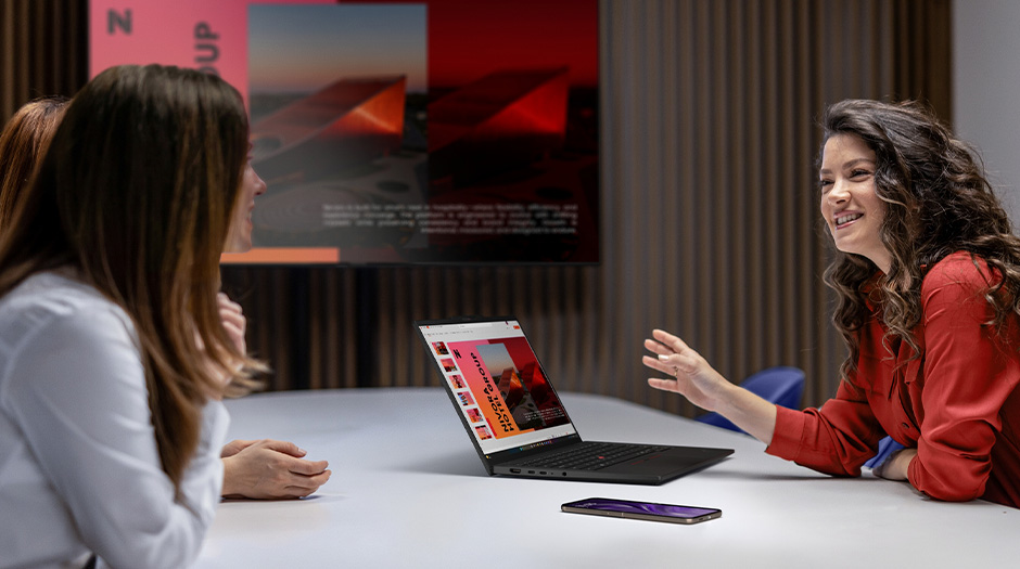 三名女性在會議桌旁圍繞著一台 Lenovo ThinkPad T14s Gen 7 (14” Intel) 筆記型電腦交談。