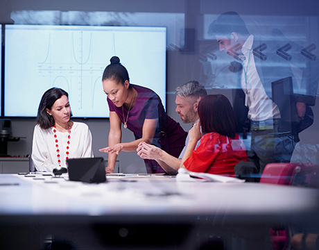 Group discussing at a conference table with a digital presentation in the background.