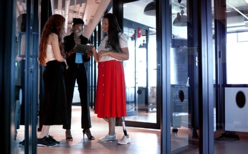 Tri ženske stojijo na hodniku in gledajo tablico, ki jo drži gospa, ki stoji zadaj.