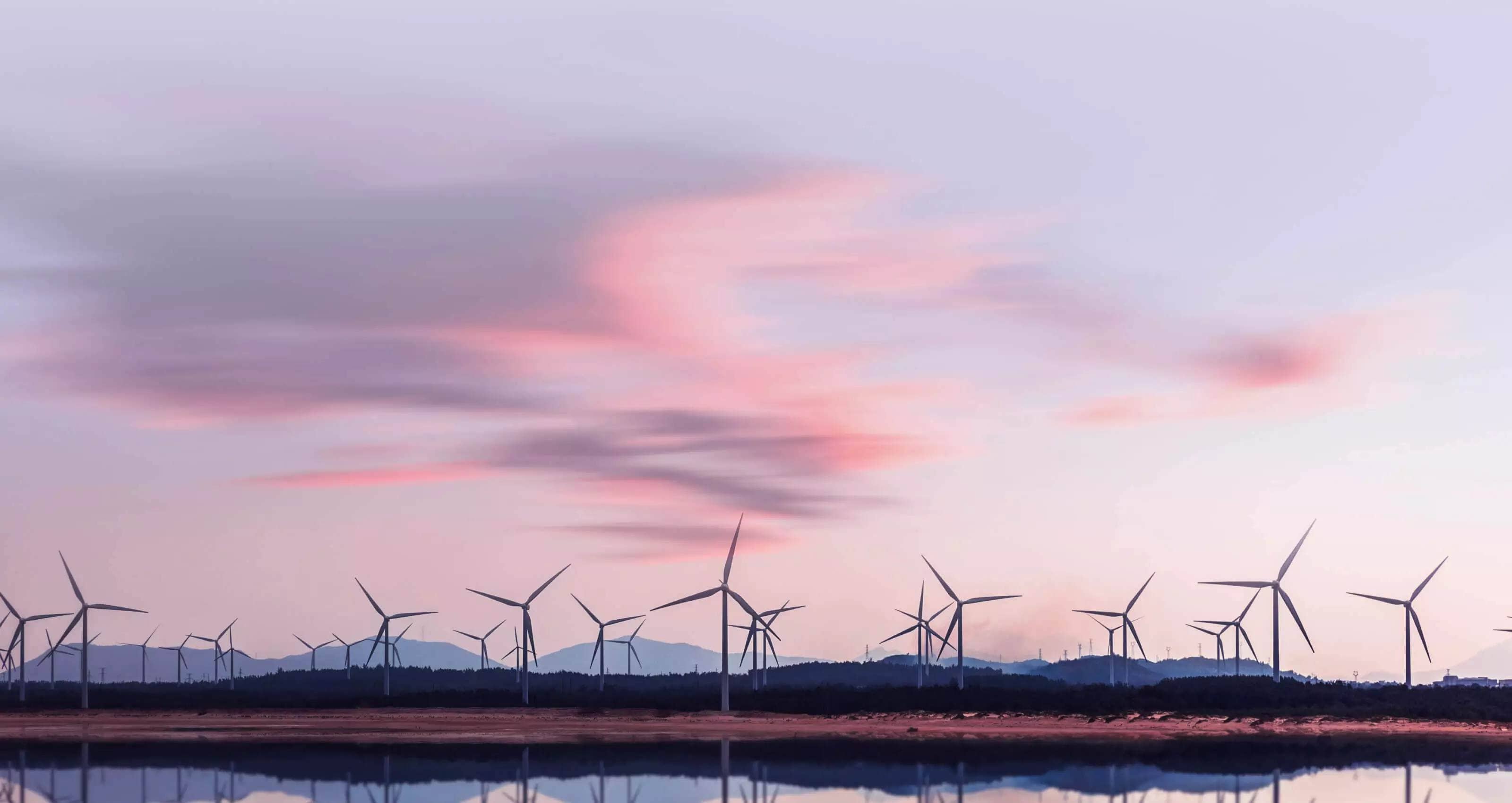Multiple windmills dotting the foreground of the image with mountains and a beautiful sunset sitting behind them.