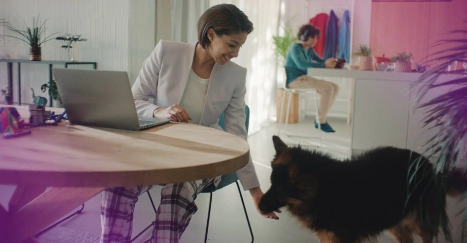 En kvinna som sitter vid ett skrivbord och deltar i ett videosamtal med flera andra på en stor Lenovo-bildskärm.