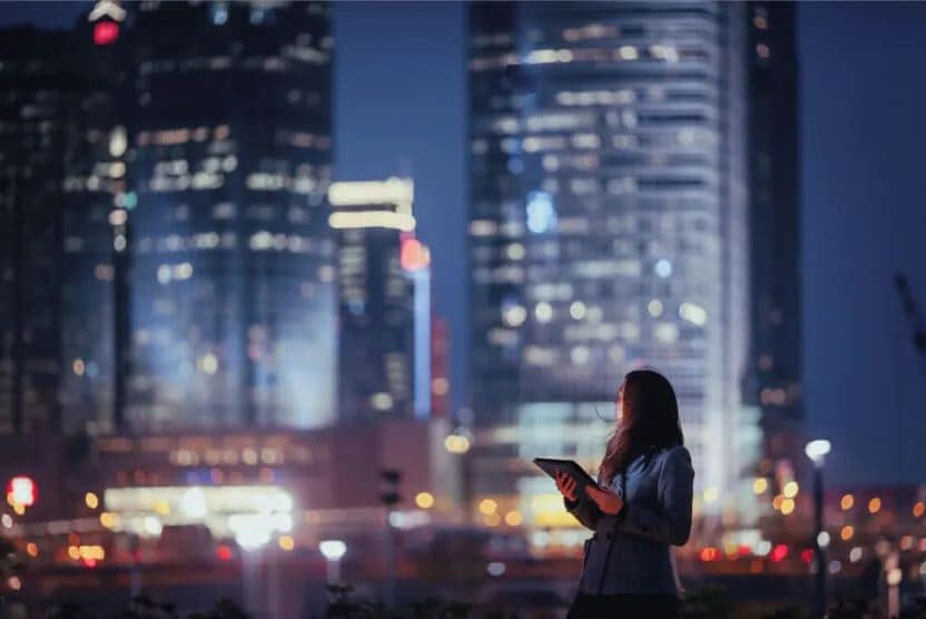 A woman standing in front of a skyscraper using a Lenovo laptop.