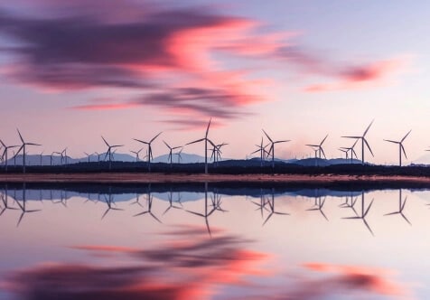 Vindkraftverk som speglas i en sjö vid solnedgången.