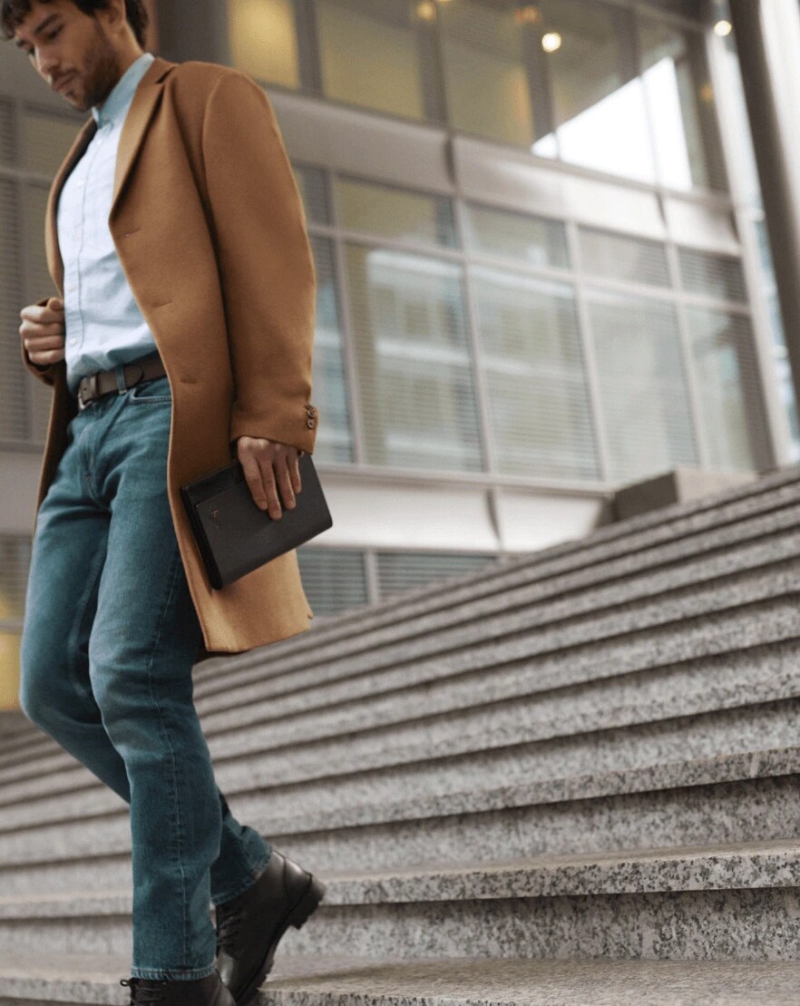 A man walking down plaza stairs carrying a folded up Lenovo ThinkPad X1 Fold in his left hand, with leather folio showing