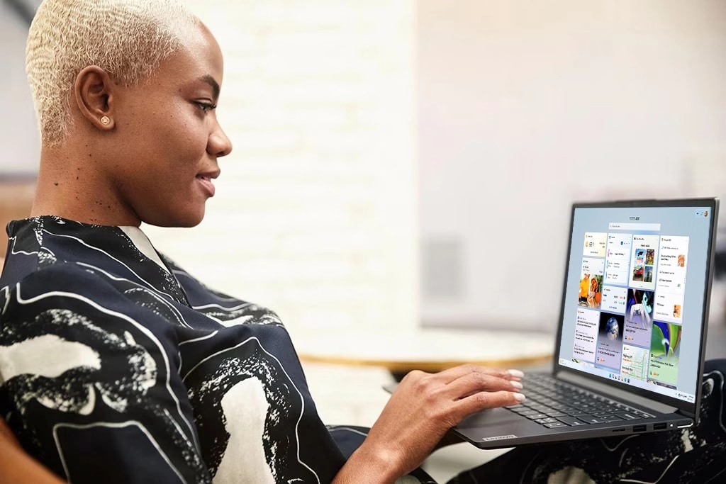 Masada otururken Yoga Slim 7, 14 inç dizüstü bilgisayarda yazı yazan bir kişi