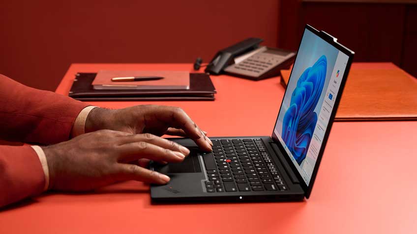 A man’s hands typing on a Lenovo laptop that’s sitting on an orange table