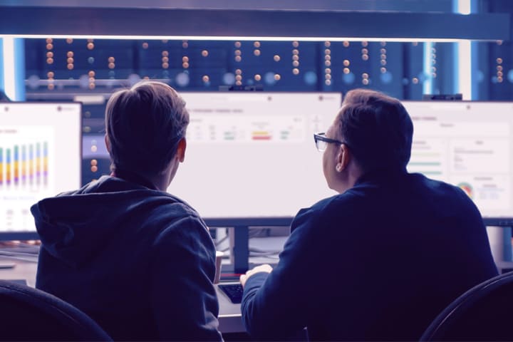 The image shows people in an office examining data on monitors. 