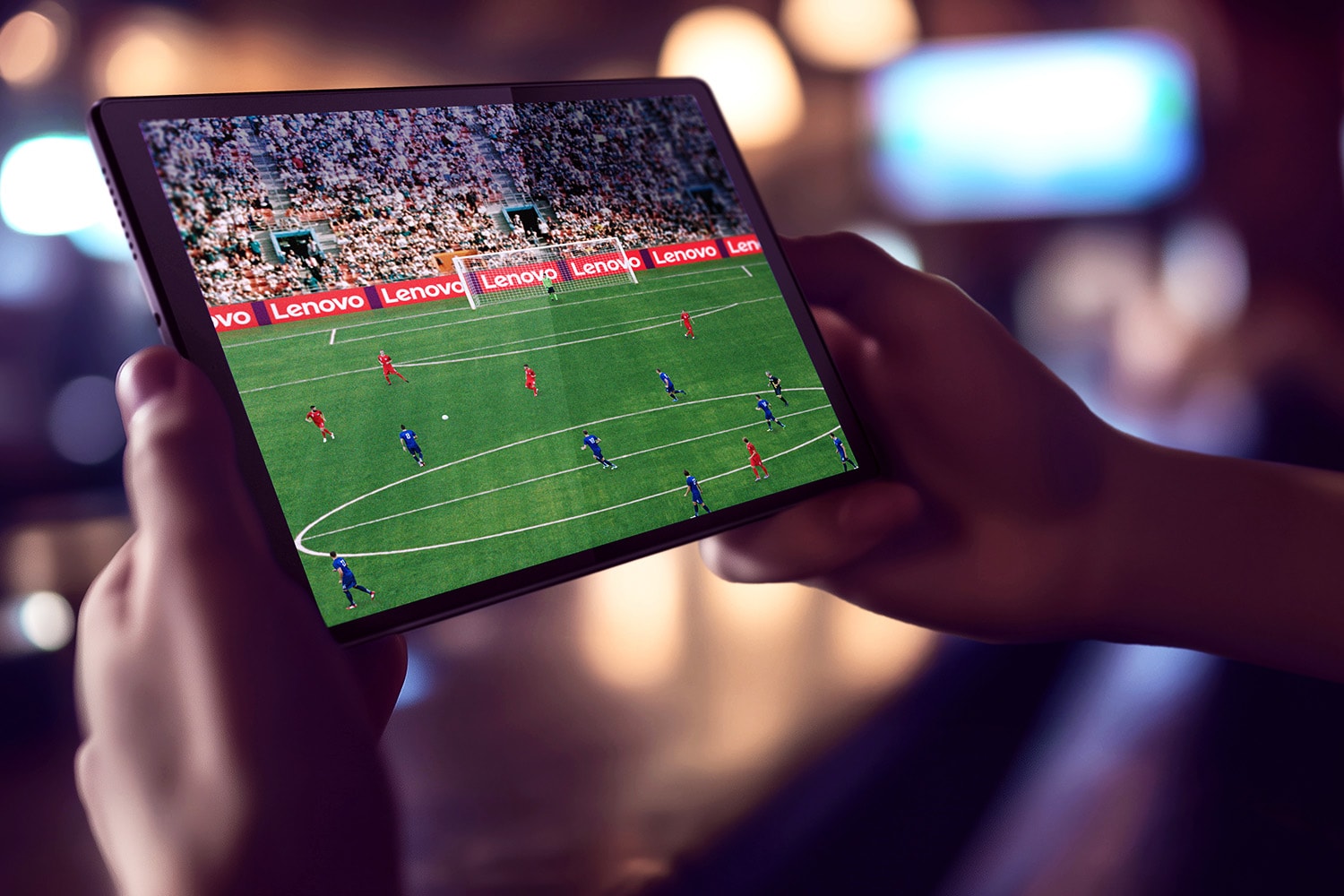 A pair of hands show a Lenovo tablet with a football event on the display.