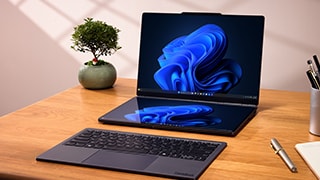 Atop a desk with a plant and various office supplies sits the Lenovo ThinkBook Modular AI PC concept with two pin-connected displays, both showing the blue Windows Bloom, and the detached keyboard sitting in front.