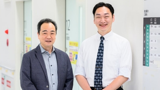 The image shows two doctors standing next to each other smiling at the camera.