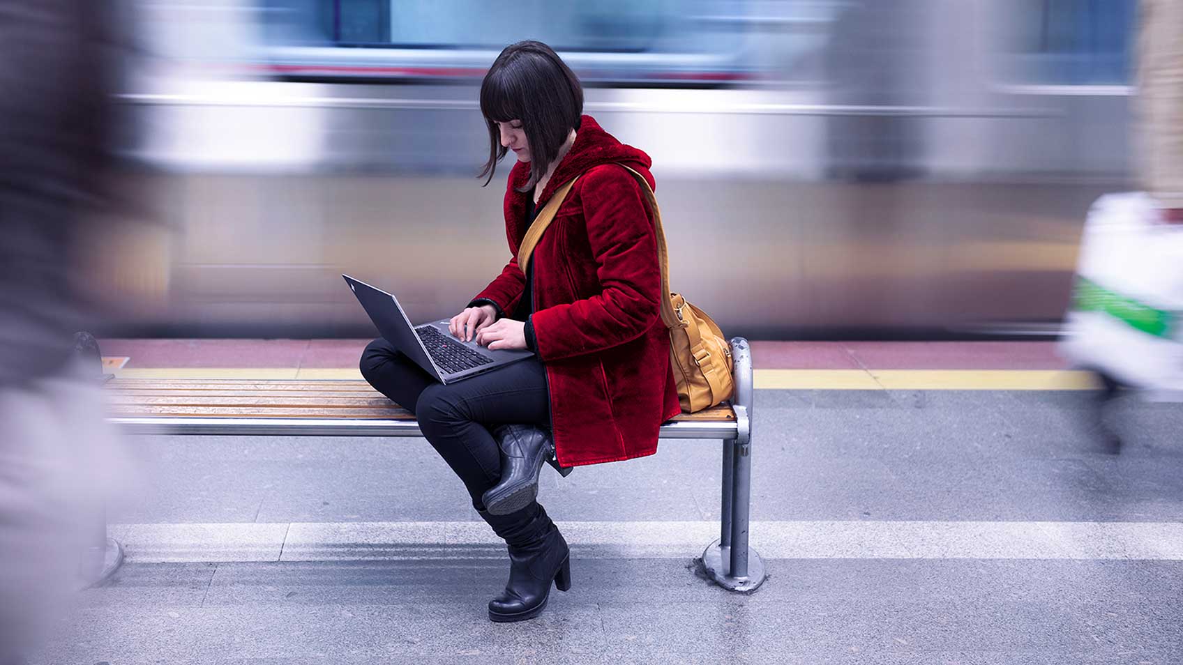 Une femme travaillant sur son portable sur un banc de métro alors qu’un train se déplace derrière elle.