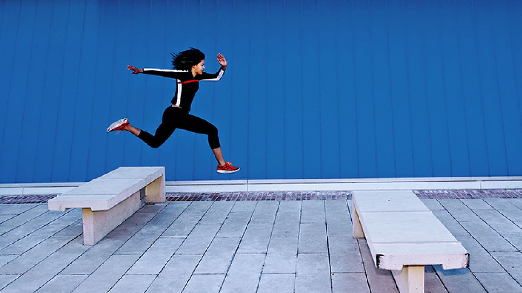 A woman leaping over concrete benches