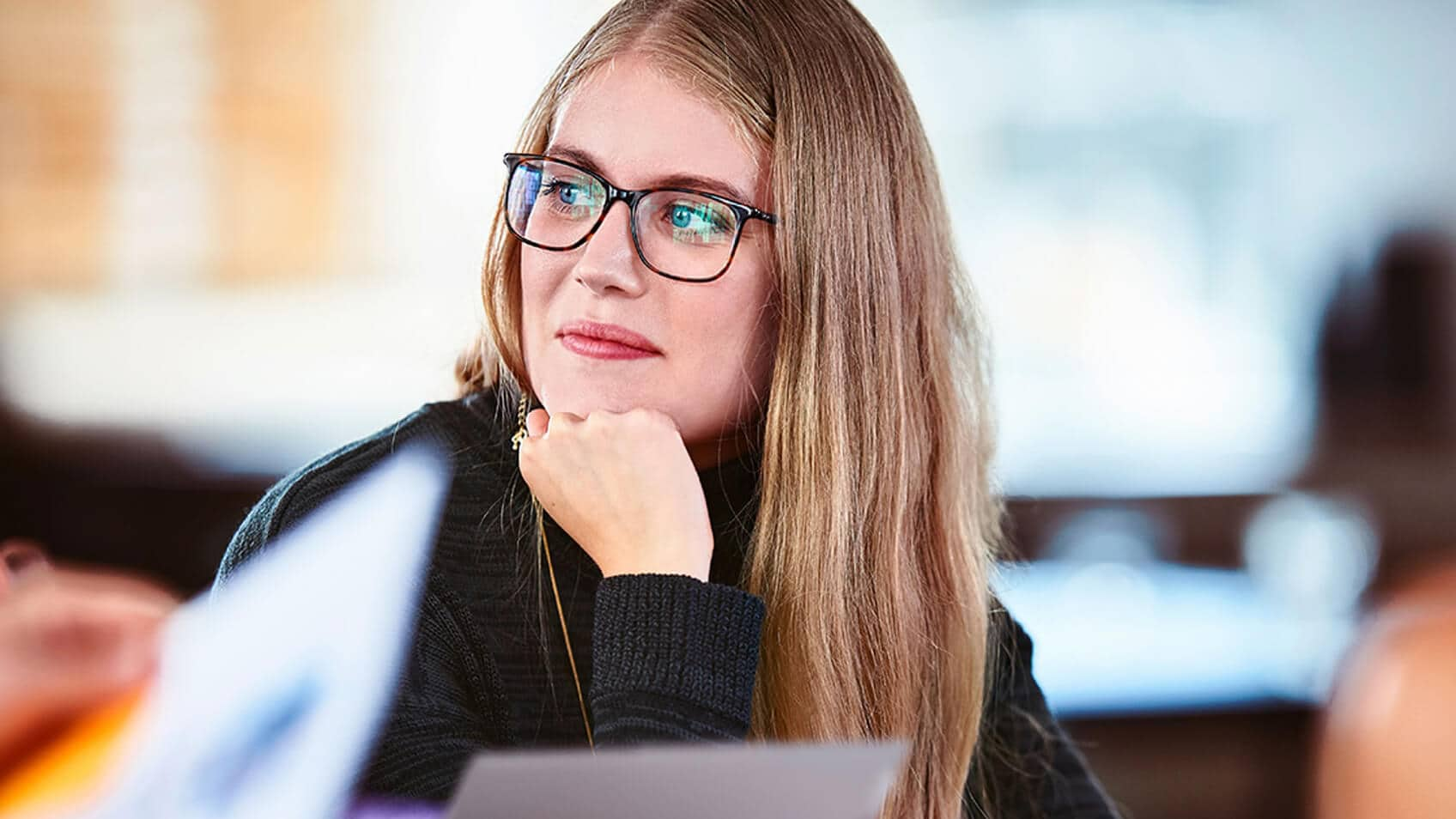 A woman wearing glasses and resting her chin on her hand