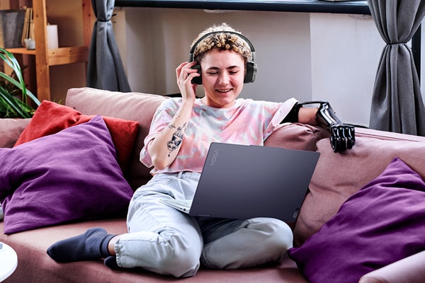 Young woman sitting on her couch working on a laptop with headsets on